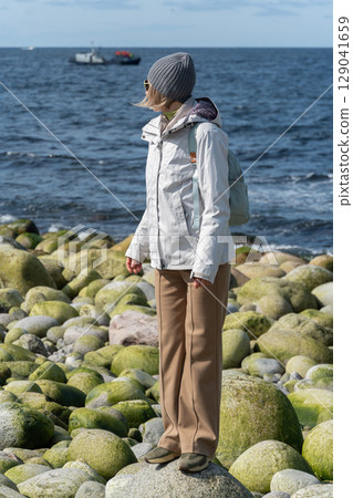 Woman in light outdoor gear standing among round greenish boulders at Dragon Egg Beach, Barents Sea in Teriberka, Arctic 129041659