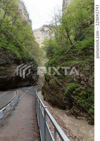 A dramatic view of Chegem Gorge with a narrow pedestrian path and road winding between towering limestone cliffs A dramatic view of Chegem Gorge with a narrow pedestrian path and road winding between towering limestone cliffs 129041743