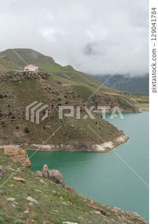 A vivid turquoise mountain lake winds through the lush, mist-covered hills of the North Caucasus A vivid turquoise mountain lake winds through the lush, mist-covered hills of the North Caucasus 129041784