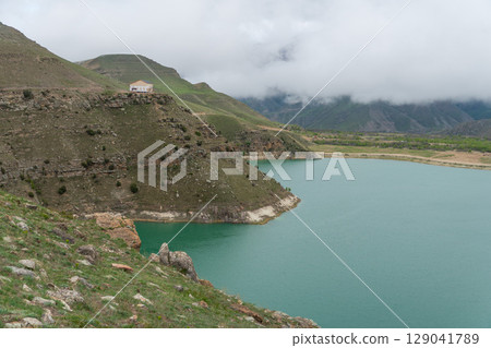 A vivid turquoise mountain lake winds through the lush, mist-covered hills of the North Caucasus A vivid turquoise mountain lake winds through the lush, mist-covered hills of the North Caucasus 129041789