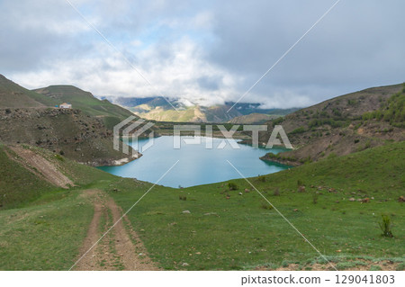 Lake Gizhgit in Kabardino-Balkaria, Russia, surrounded by rolling green hills and partially covered by low-hanging clouds 129041803