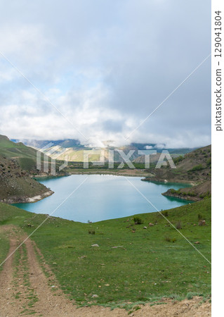 Lake Gizhgit in Kabardino-Balkaria, Russia, surrounded by rolling green hills and partially covered by low-hanging clouds 129041804