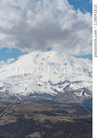 Mount Elbrus covered in snow rises majestically under a dramatic cloud-filled sky in Kabardino-Balkaria, Russia Mount Elbrus covered in snow rises majestically under a dramatic cloud-filled sky in Kabardino-Balkaria, Russia 129041815
