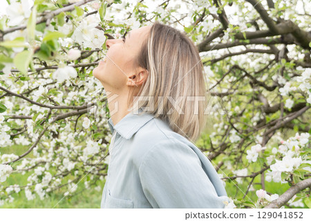 Joyful middle-aged woman in a light blue outfit smiling. Wellness brands, skincare and fragrance advertising, or nature retreat promotions 129041852