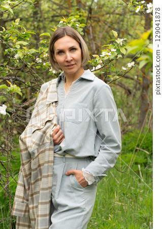Confident middle-aged woman in a light blue outfit with a plaid coat over her shoulder. Fashion branding, eco-conscious lifestyle, mature self-expression. 129041878