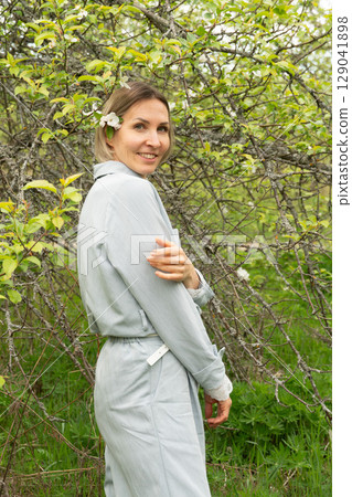 Confident middle-aged woman in light blue clothing smiling in a spring orchard. Personal care, skincare, and wellness industries may use this image to convey natural beauty and authenticity 129041898