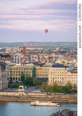 A panoramic view of Budapest with a red-and-white hot air balloon floating above the city skyline at sunset A panoramic view of Budapest with a red-and-white hot air balloon floating above the city skyline at sunset 129041968