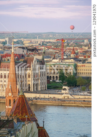 A panoramic view of Budapest with a red-and-white hot air balloon floating above the city skyline at sunset A panoramic view of Budapest with a red-and-white hot air balloon floating above the city skyline at sunset 129041970