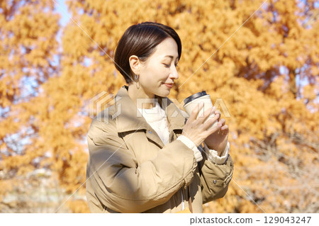 Middle-aged woman drinking coffee outdoors, autumn leaves Middle-aged woman drinking coffee outdoors, autumn leaves 129043247