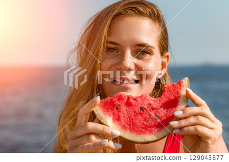 Watermelon Woman Summer Beach: Happy woman enjoys refreshing watermelon slice by seaside on sunny day. 129043877