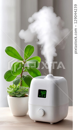 Modern air humidifier with digital display next to potted green plants on wooden table 129044239