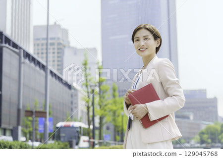 Portrait of a young businesswoman standing in an office district with a red notebook 129045768