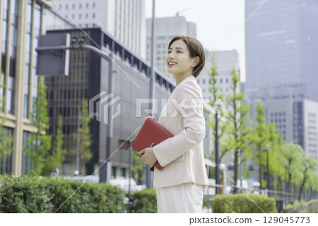 Portrait of a young businesswoman standing in an office district with a red notebook 129045773