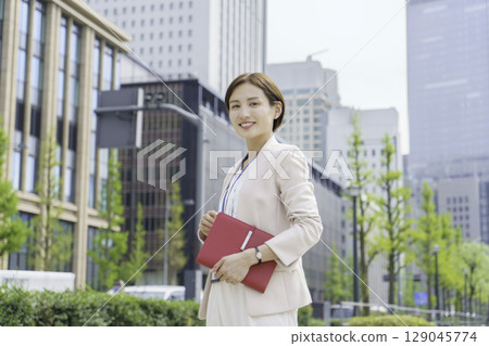 一位年輕女商人站在辦公區,手裡拿著一本紅色筆記本的畫像 一位年輕女商人站在辦公區,手裡拿著一本紅色筆記本的畫像 129045774