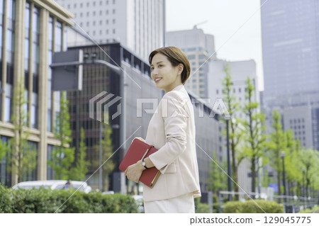 Portrait of a young businesswoman standing in an office district with a red notebook 129045775