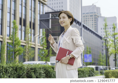 一位年輕女商人站在辦公區，手裡拿著一本紅色筆記本的畫像 129045777