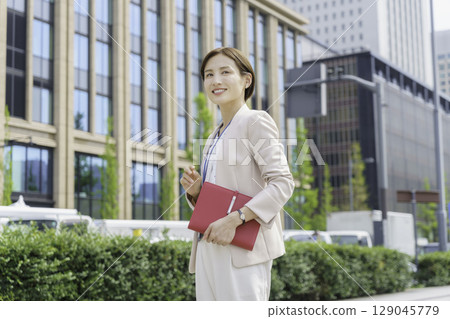 Portrait of a young businesswoman standing in an office district with a red notebook 129045779