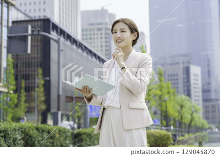 Portrait of a young businesswoman standing with a notebook in an office district Portrait of a young businesswoman standing with a notebook in an office district 129045870