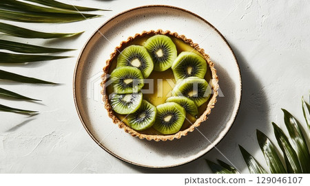Tropical fruit tart with kiwi and mango arranged over a glossy citrus glaze on a stone surface 129046107