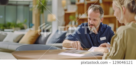 Professional furniture consultant assists customer in modern showroom with fabric samples 129046121