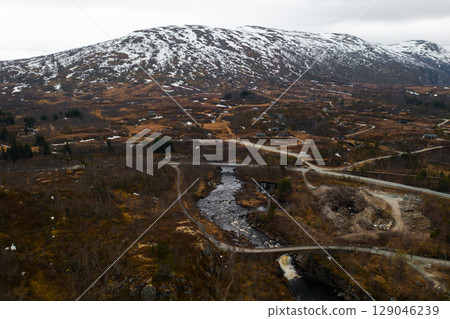 Majestic canyon leads to Voringsfossen revealing towering rugged cliffs and winding river. Distant mountains frame dramatic vast Norwegian landscape 129046239