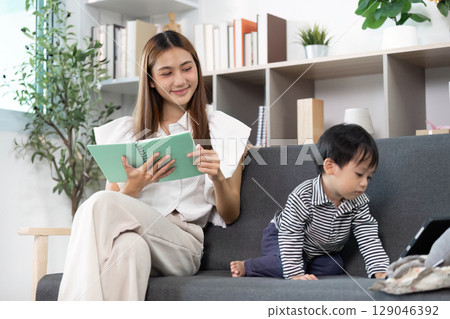 Digital Play. Caregiver and toddler engaging with a notebook and tablet in a modern living room. 129046392