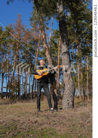 Portrait of smiling caucasian artist plays wooden acoustic guitar in autumnal park. Young songwriter plays string musical instrument hobby outside in nature fall time. Audio music healing 129046461