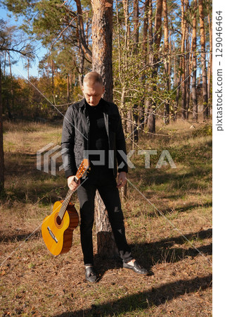 Portrait of smiling caucasian artist plays wooden acoustic guitar in autumnal park. Young songwriter plays string musical instrument hobby outside in nature fall time. Audio music healing Portrait of smiling caucasian artist plays wooden acoustic guitar in autumnal park. Young songwriter plays string musical instrument hobby outside in nature fall time. Audio music healing 129046464