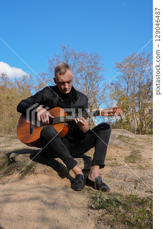 Blonde man playing string guitar outdoors in autumn forest. Concept of sound therapy, mental health and wellness rituals. Calmness tranquility audio-sensory practices. Aura farming energy Blonde man playing string guitar outdoors in autumn forest. Concept of sound therapy, mental health and wellness rituals. Calmness tranquility audio-sensory practices. Aura farming energy 129046487