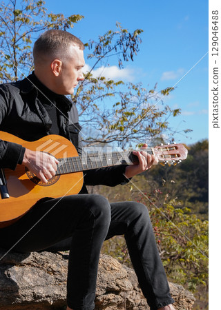 Portrait of smiling caucasian artist plays wooden acoustic guitar in autumnal park. Young songwriter plays string musical instrument hobby outside in nature fall time. Audio music healing 129046488