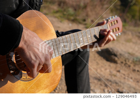 Close up hands of artist plays wooden acoustic guitar in autumnal park. Young songwriter plays string musical instrument hobby outside in nature fall time. Audio music healing 129046493