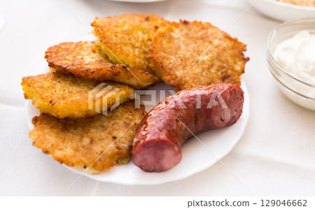 Fried grated potato pancakes with fried sausage on white plate 129046662