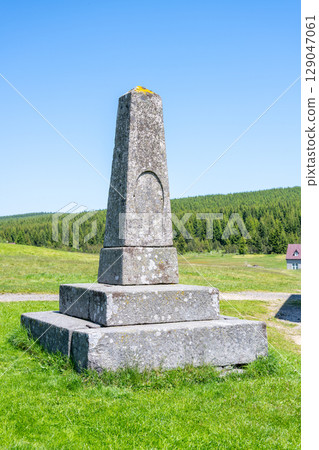 A stone pyramid stands proudly in Jizerka Village, surrounded by lush green mountains and blue skies. It is a notable landmark in the Czech Republic, attracting visitors all year round. 129047061