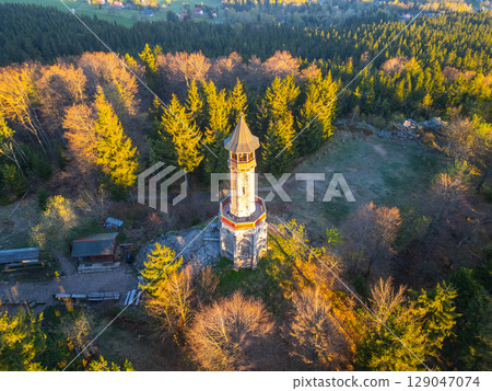 Basking in the morning light, Stepanka Lookout Tower stands tall amidst the lush greenery of the Jizera Mountains. The tranquil landscape of Korenov offers a serene escape into nature. 129047074