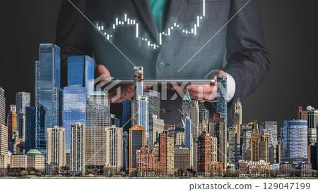 businessman hand writing on paper with graph chart and pen on city background with city buildings, skyscrapers and skyscrapers 129047199