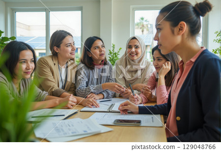 Group of diverse businesswomen listening to female leader during team meeting in modern office. Women collaborating on strategy together Group of diverse businesswomen listening to female leader during team meeting in modern office. Women collaborating on strategy together 129048766