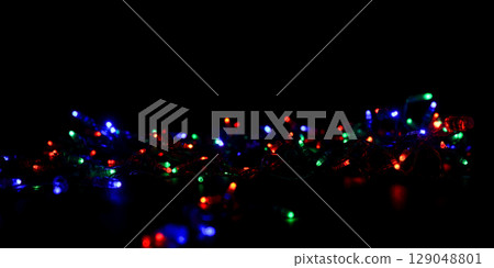 Messy jumble of multicolor christmas lights on black background, festive holiday decoration with red, green, and blue colors overlay Messy jumble of multicolor christmas lights on black background, festive holiday decoration with red, green, and blue colors overlay 129048801