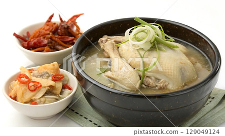 Close up of samgyetang in a black bowl with side dishes on a white table 129049124