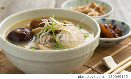 A bowl of chicken soup with mushrooms and garnish on a bamboo placemat near 129049125