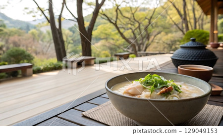 A bowl of soup on a table with a view of trees and benches in the background 129049153