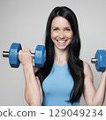 A woman in a blue dress doing dumbbell training 129049234