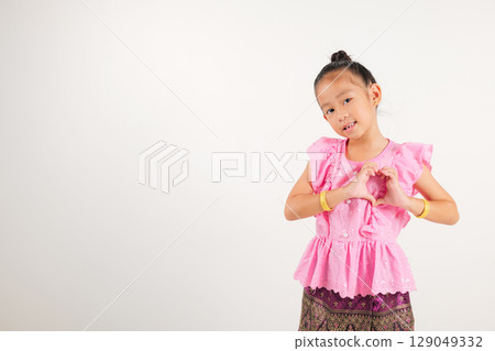 Portrait Thailand kid girl smiling traditional Thai dress costume shows creating heart shape with fingers and hands, studio isolated white background, kindergarten child sending love for Valentine day 129049332