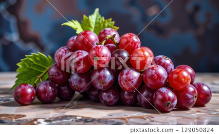 Red grape cluster with green leaves on patterned surface, fresh and vibrant closeup artistic fruit study with natural light Red grape cluster with green leaves on patterned surface, fresh and vibrant closeup artistic fruit study with natural light 129050824