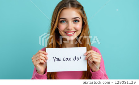 Confident girl holding motivational sign with positive message smiling happily against blue background 129051129