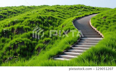 Curved staircase embedded in lush green grass on hill under clear sky, creating peaceful and natural outdoor scene 129051207