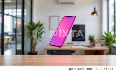 Smartphone with pink screen floating above wooden table in modern office with plants and computer Smartphone with pink screen floating above wooden table in modern office with plants and computer 129051243