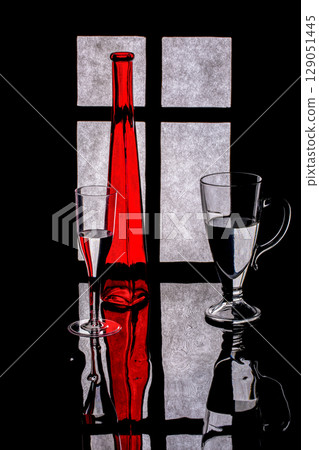 Still life with a red bottle and glasses with liquid on a window background 129051445