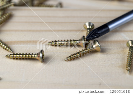 screwdriver and screws for fixing wood lying on a board, a group of tools for construction , close up screwdriver and screws for fixing wood lying on a board, a group of tools for construction , close up 129051618