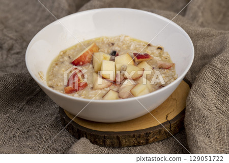 adding pieces of peach to hot oatmeal , quickly cooked oatmeal porridge with dried fruits and berries and pieces of fresh peach, close up 129051722