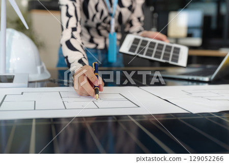 Architect woman working with blueprints for sketching a construction project, green energy and solar panel concept. 129052266
